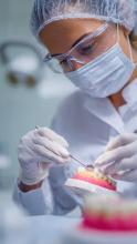 Female dentist wearing blue surgical cap, protective mask, and gloves intently working on pink dental model tray in sterile clinic environment, showcasing precision dental care in Gurgaon.