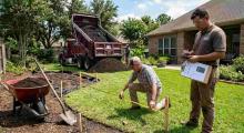 Homeowner measuring backyard to calculate cubic yards for bulk soil delivery before landscaping project in Houston TX